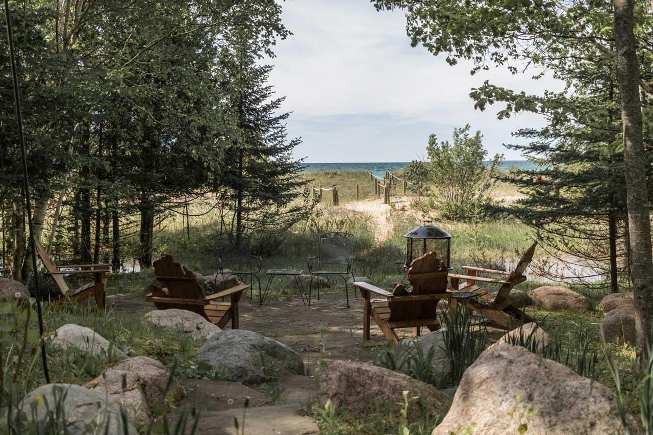 A rustic outdoor seating area with wooden chairs and a table, overlooking a beach.