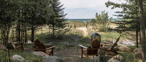 A rustic outdoor seating area with wooden chairs and a table, overlooking a beach.