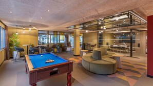 A pool table in a modern lounge area with comfortable seating and a glass partition.