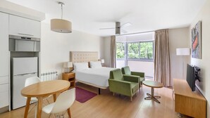 A hotel room with a bed, a desk, a chair, a small table, a television, and a window with curtains.