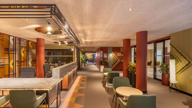 A modern hotel lobby with a reception desk, seating area, and a staircase.