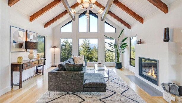 A spacious living room with a high ceiling, large windows, a fireplace, and a modern sofa.