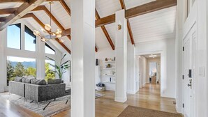 A spacious living area with a high ceiling, wooden beams, a large window, and a cozy seating area.