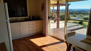 A kitchen with wooden flooring, a refrigerator, and a window overlooking a garden with a view of wind turbines.