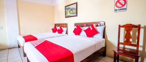 A hotel room with two beds, a wooden chair, a ceiling fan, a painting on the wall, and a 'No Smoking' sign.