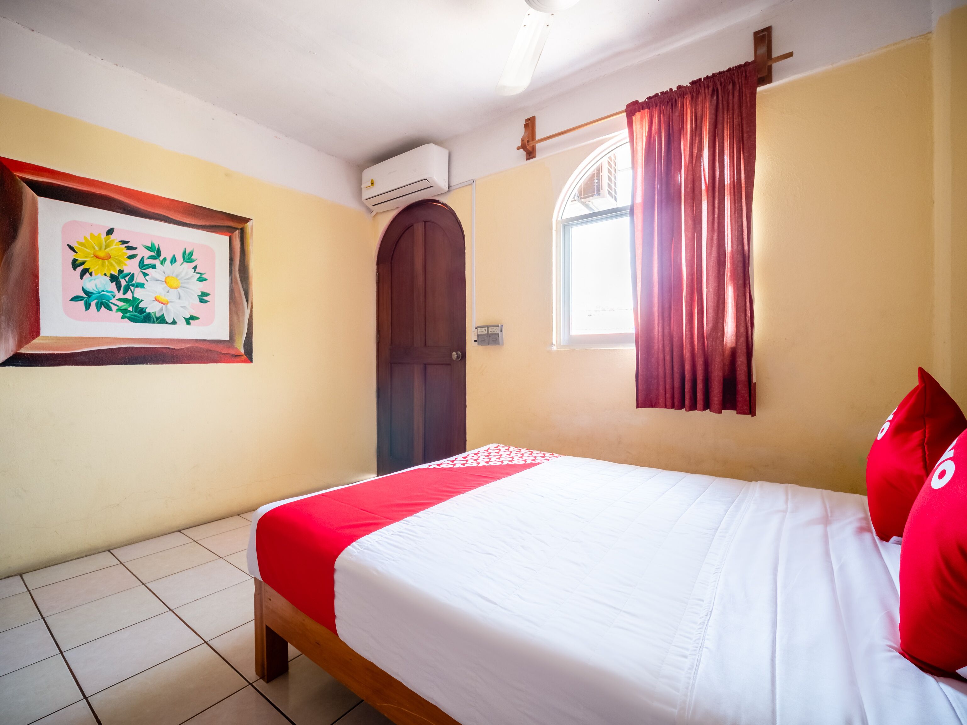 A bedroom with a bed, a window with curtains, an air conditioning unit, and a door.