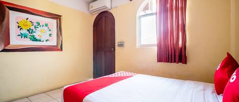Un dormitorio con cama, ventana con cortinas, aire acondicionado y puerta.