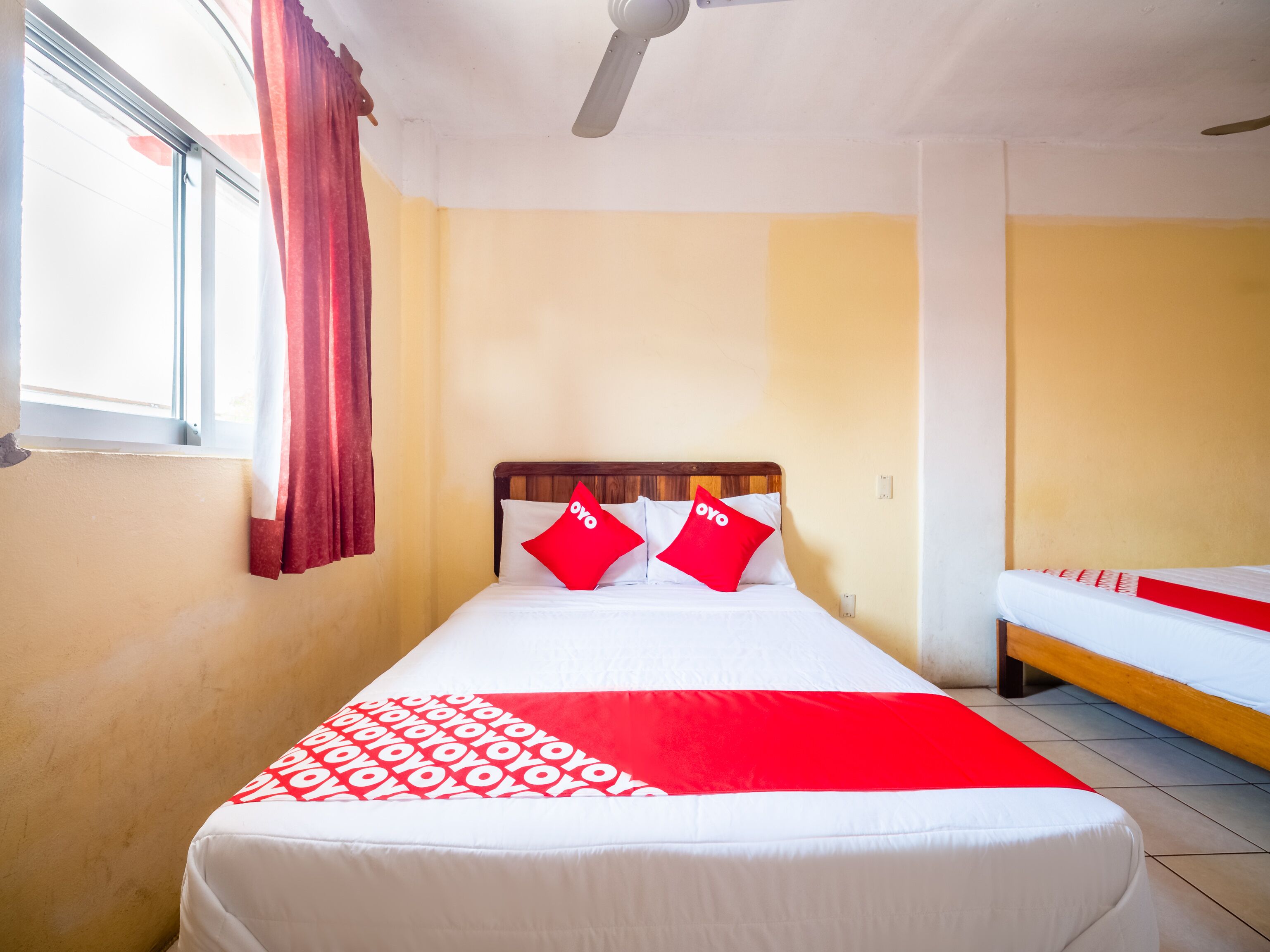 Habitación de hotel con cama, ventana con cortinas, ventilador de techo y mesita de noche.