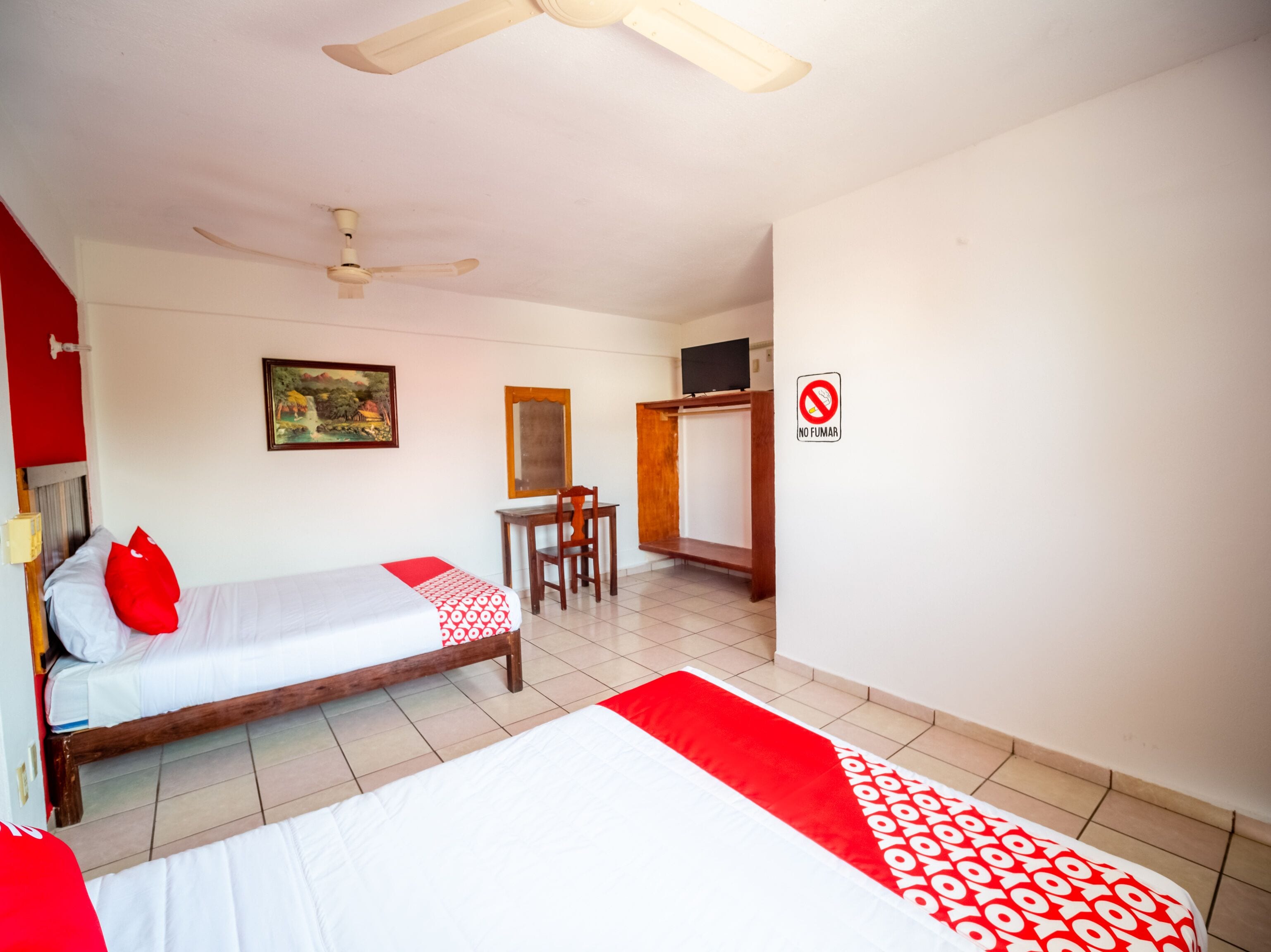 A room with two beds, a desk, a chair, a television, and a no-smoking sign.