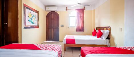 A hotel room with two beds, a ceiling fan, a window with curtains, and a door.