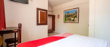 A hotel room with a bed, a desk, a chair, a TV, a painting, and a door.