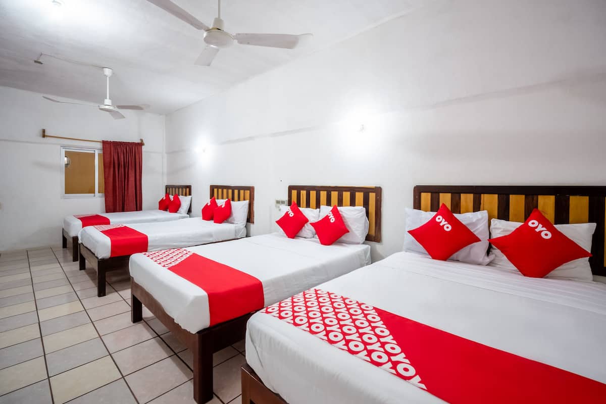 Ein Hotelzimmer mit vier Einzelbetten, jeweils mit einem Holz-Kopfteil, weißer Bettwäsche und roten Akzenten.