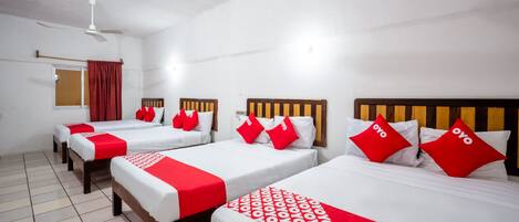 Een hotelkamer met vier éénpersoonsbedden, elk voorzien van een rood-witte spreideken en bijpassende kussens.