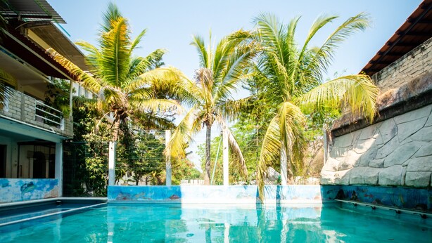 A swimming pool with clear blue water, surrounded by palm trees and a stone wall. - OYO Hotel Betsua Vista Hermosa, Huatulco (Santa María Huatulco)