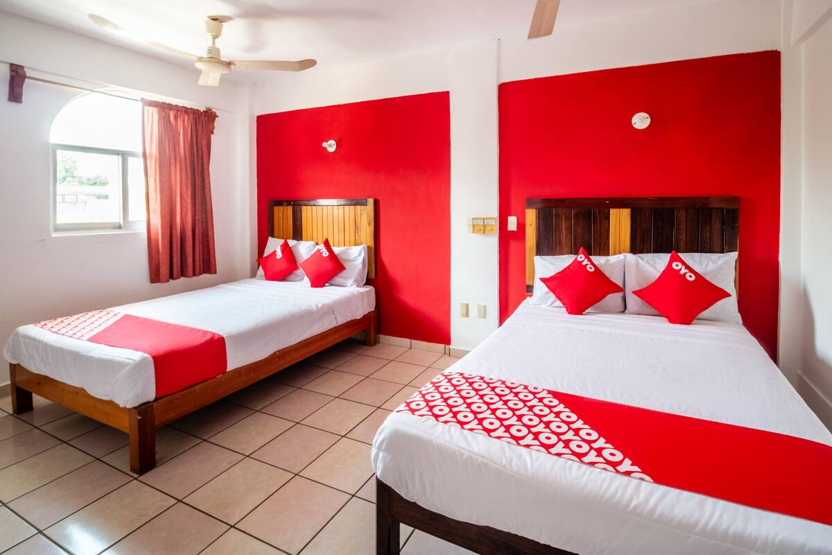 Ein Hotelzimmer mit zwei Betten, roten Wänden, weißer Bettwäsche und Deckenventilatoren.