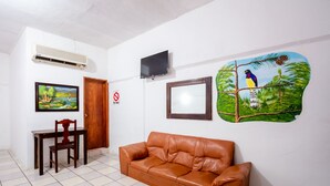 A room with a brown leather sofa, a wooden chair, a desk with a chair, a TV mounted on the wall, and a painting of a bird on a branch. - OYO Hotel Betsua Vista Hermosa, Huatulco (Santa María Huatulco)