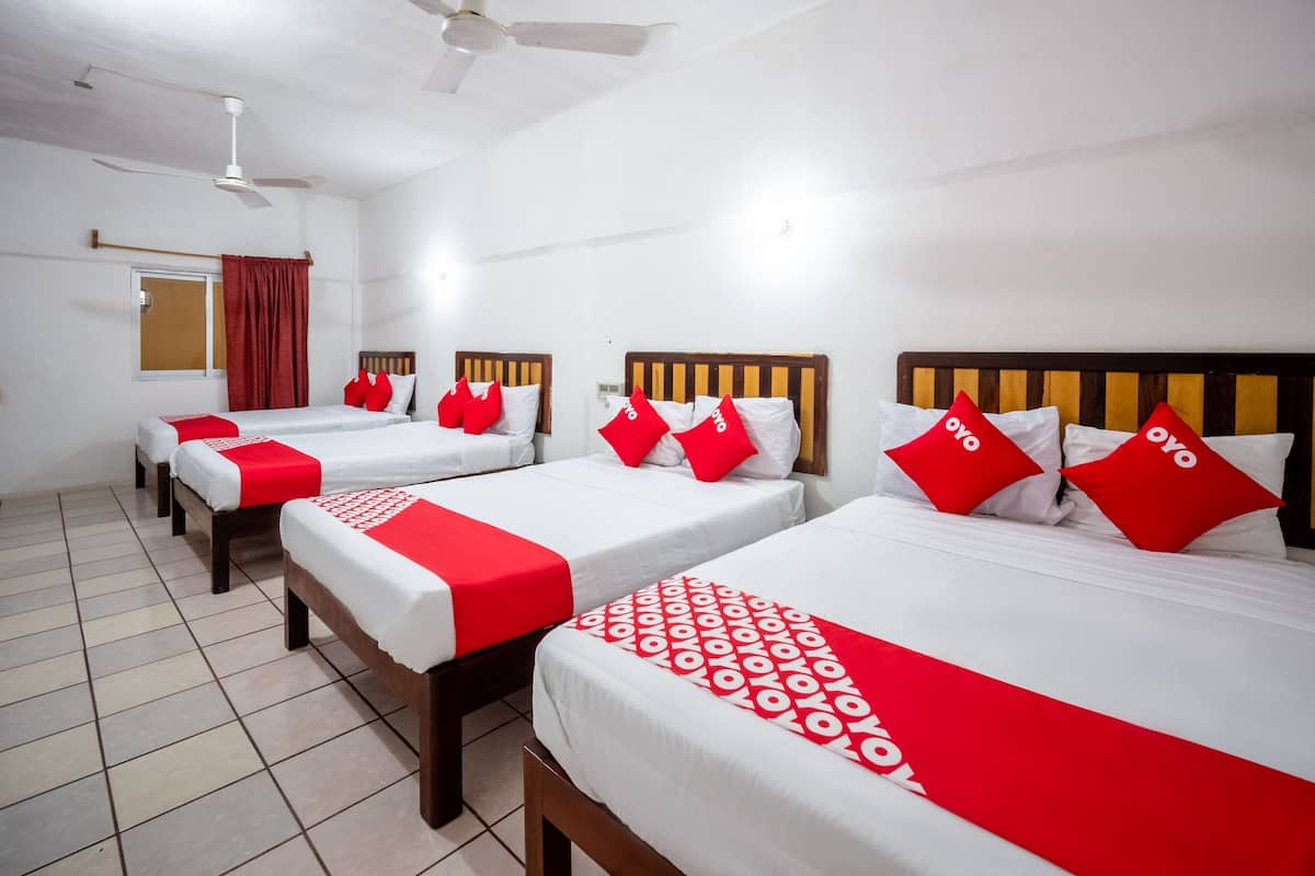Ein Hotelzimmer mit vier Betten, jedes mit einem hölzernen Kopfteil, weißer Bettwäsche und roten Akzenten.