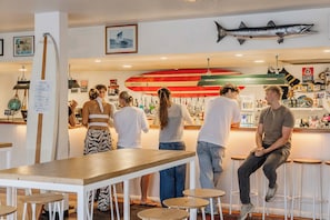 A bar area with a counter, stools, and a group of people. - The Surf House - Hostel (Byron Bay)