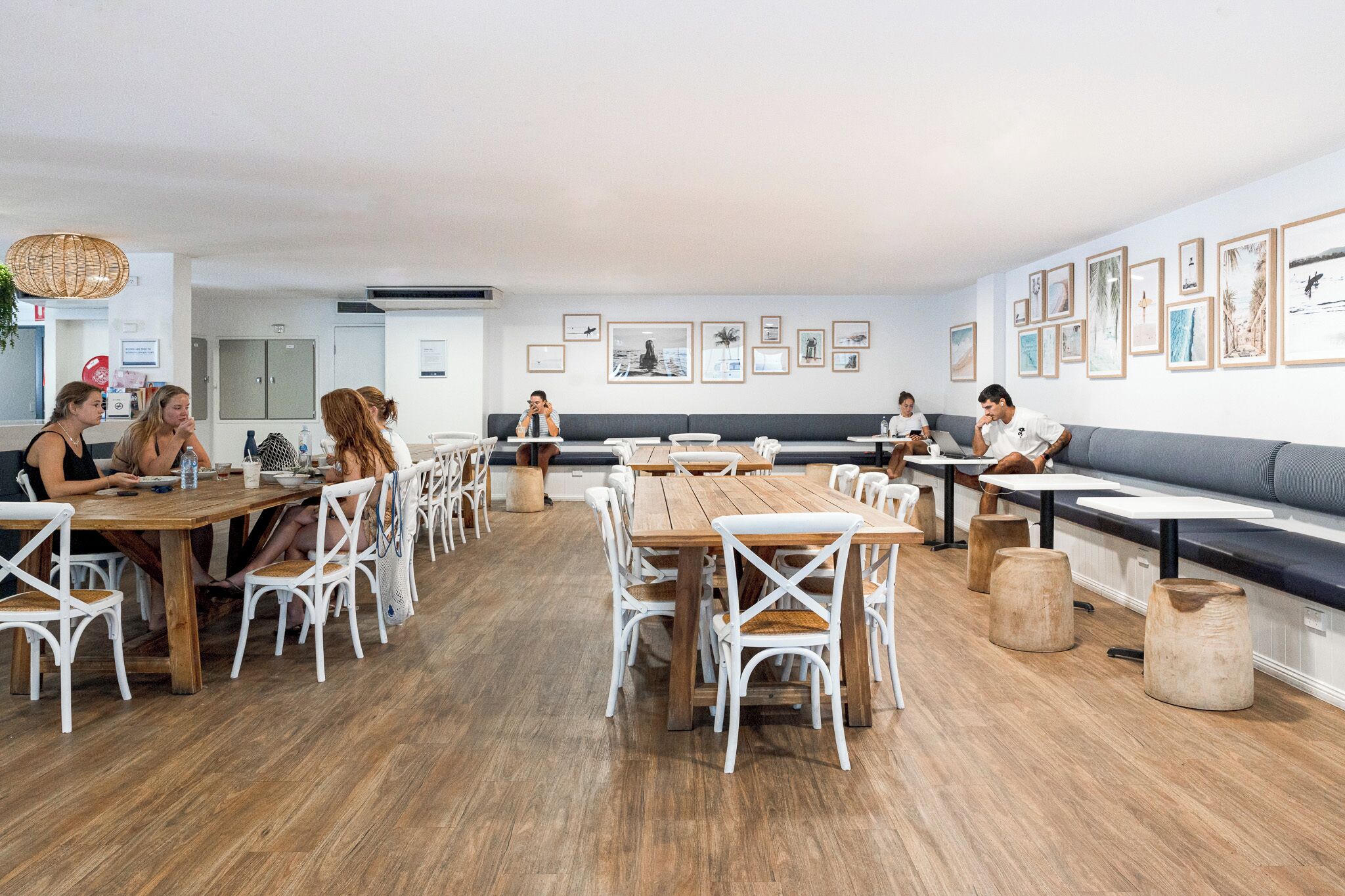 A modern dining area with wooden tables and white chairs, a long bench, and framed pictures on the walls.