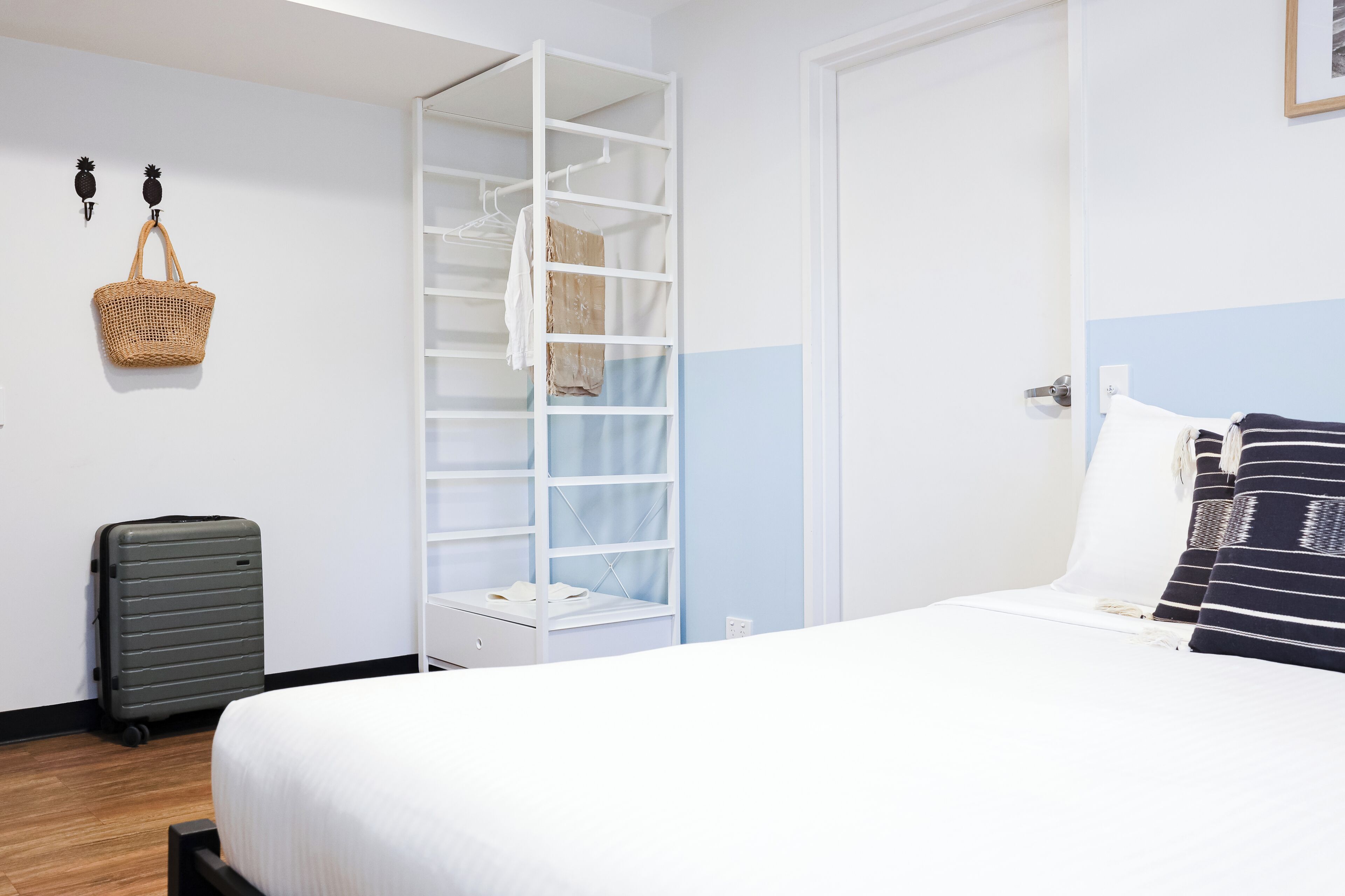 A hotel room with a bed, a wardrobe, a suitcase, and a wall-mounted basket.