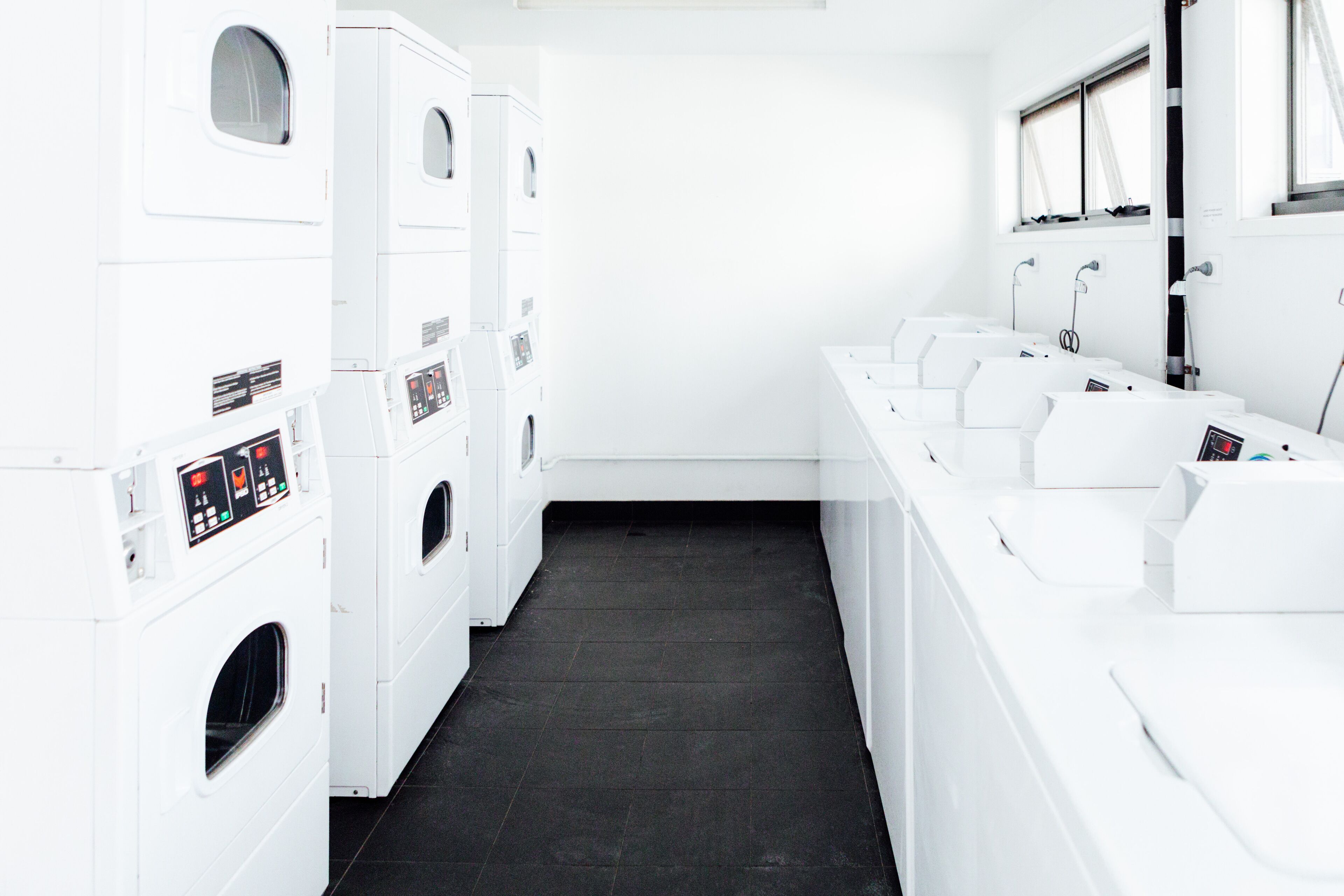 A laundry facility with multiple washing machines and dryers, a black tiled floor, and a row of sinks.