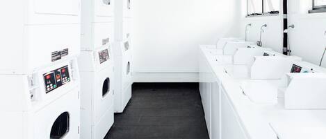 A laundry facility with multiple washing machines and dryers, a black tiled floor, and a row of sinks.
