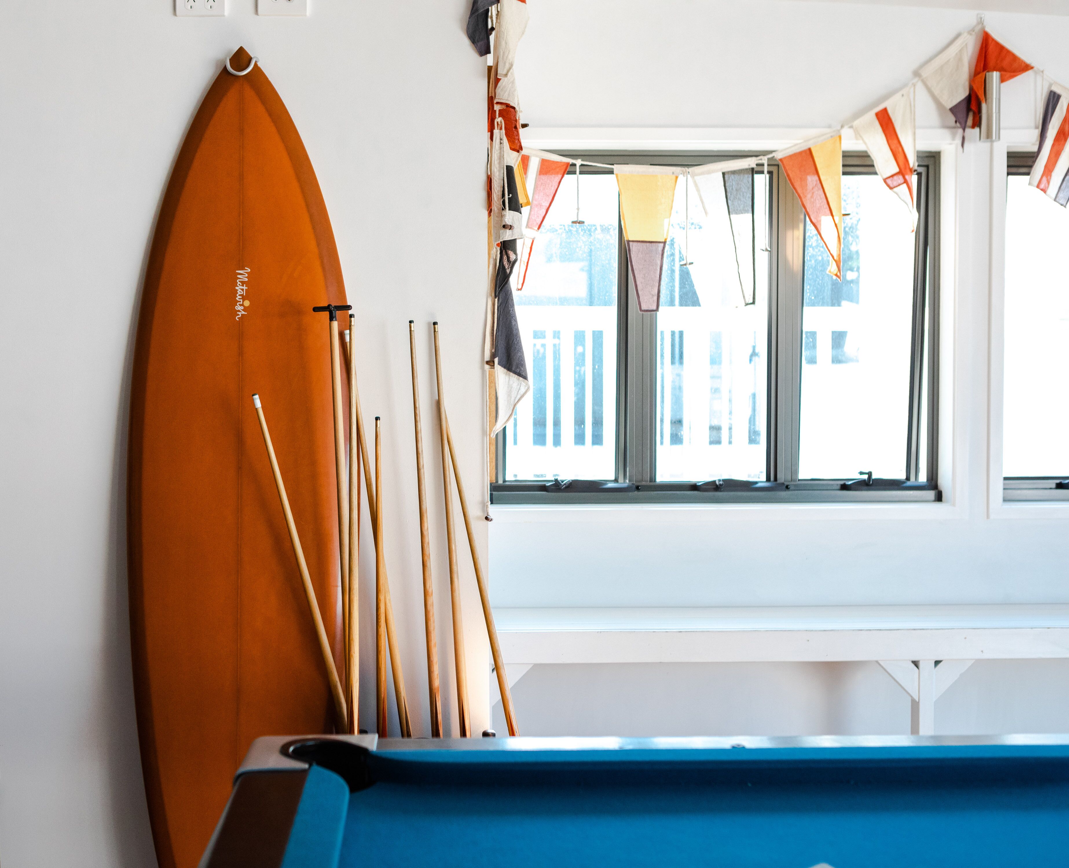A pool table with a wooden paddle and several pool cues leaning against a wall.