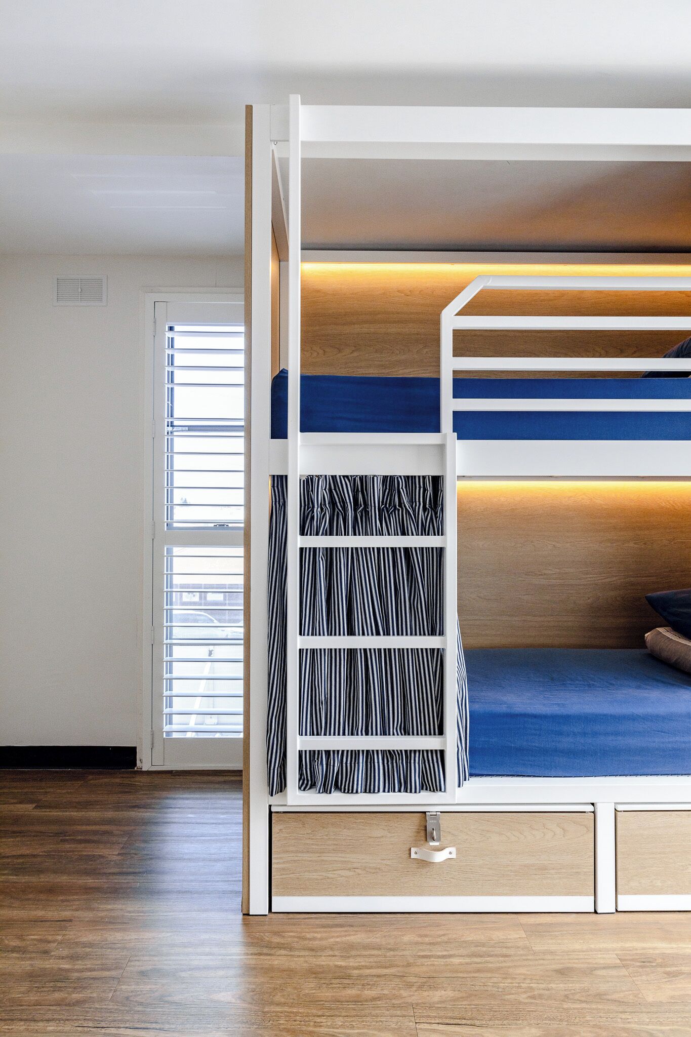 A bunk bed with a wooden headboard, a striped shelf, and a blue mattress.