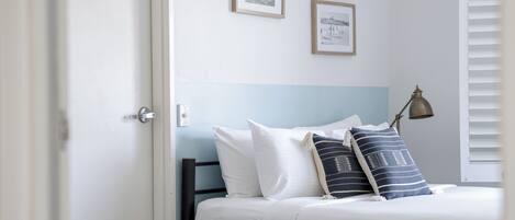 Ein Schlafzimmer mit einem Bett, weißen Kissen, einem blauen Kopfteil und zwei gerahmten Bildern an der Wand.