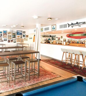 Zona bar moderna con tavolo da biliardo, sgabelli da bar e diverse immagini incorniciate alle pareti.