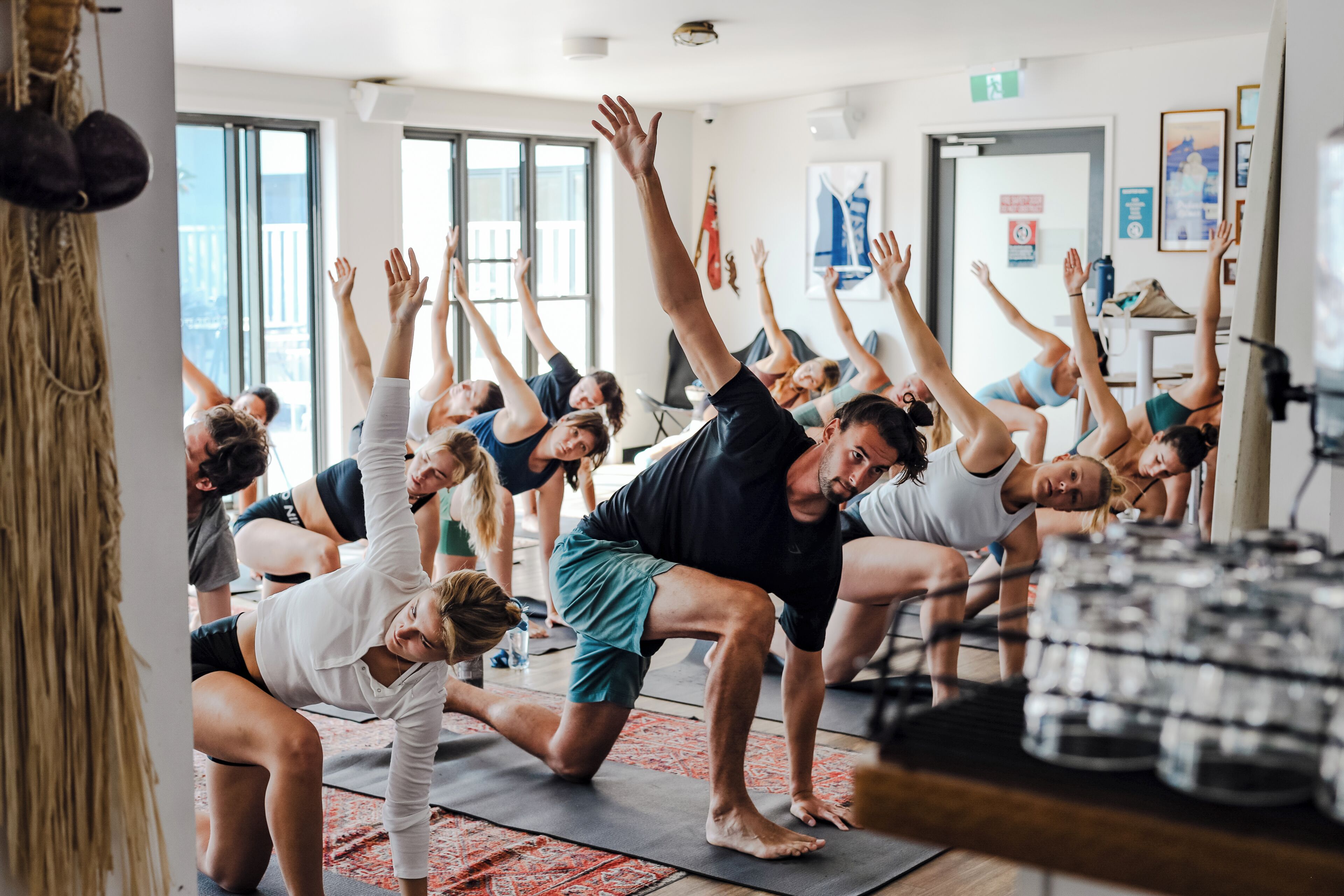 Un grupo de personas en una clase de yoga, con colchonetas en el suelo y una ventana al fondo.