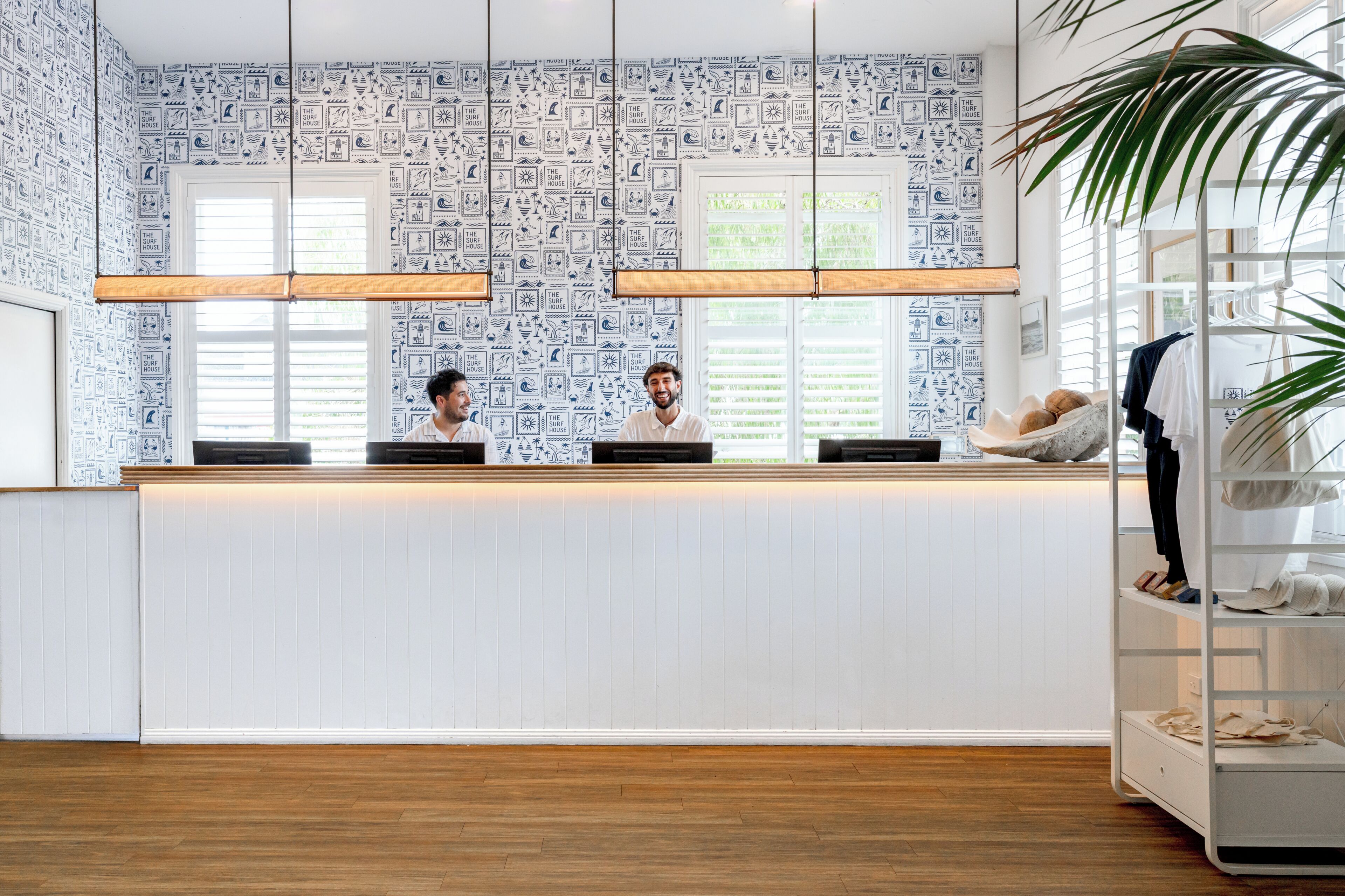 A reception desk with a patterned wallpaper, a wooden floor, and a plant on the right.