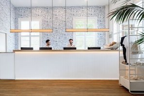 Un comptoir d’accueil avec un papier peint à motifs, un plancher en bois et une plante sur la droite.
