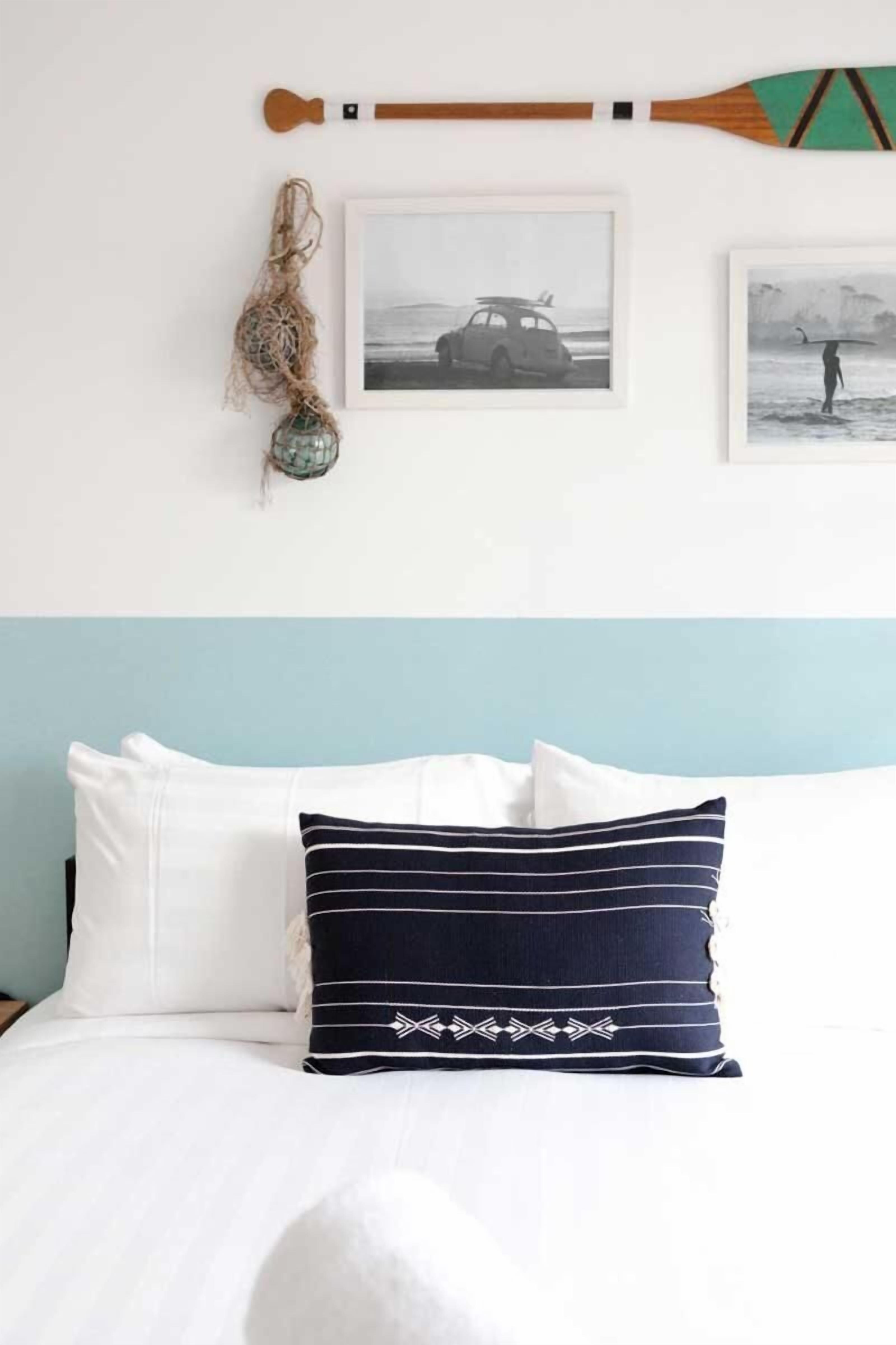 Un lit avec des oreillers blancs et bleu marine, une tête de lit en bois et deux tableaux encadrés accrochés au mur.