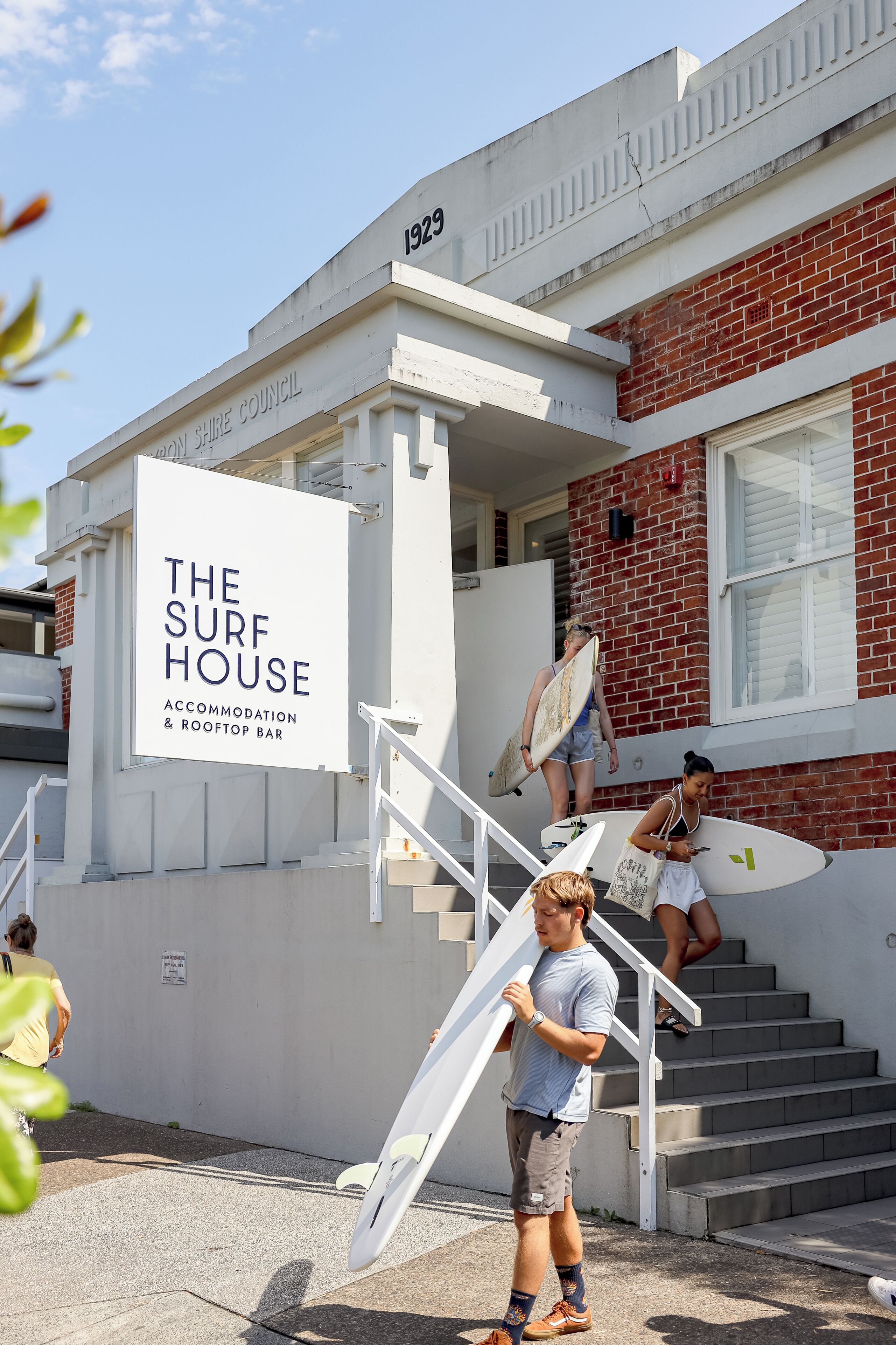 En bygning med et skilt, der viser 'The Surf House', og som indikerer en surfbutik og tagbar.