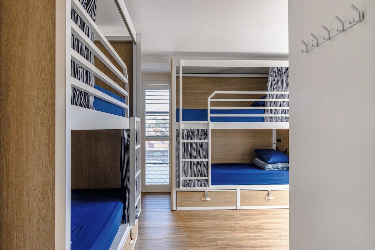 A bunk bed room with a wooden floor, a window with blinds, and a wall-mounted hook.