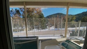 Vista da un balcone con zanzariera e ringhiera metallica, con un'area salotto coperta e un parcheggio sullo sfondo.