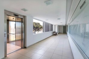 Experience the contemporary design aesthetic of this stylish hallway, featuring a glass elevator, large windows, and a cozy seating area.