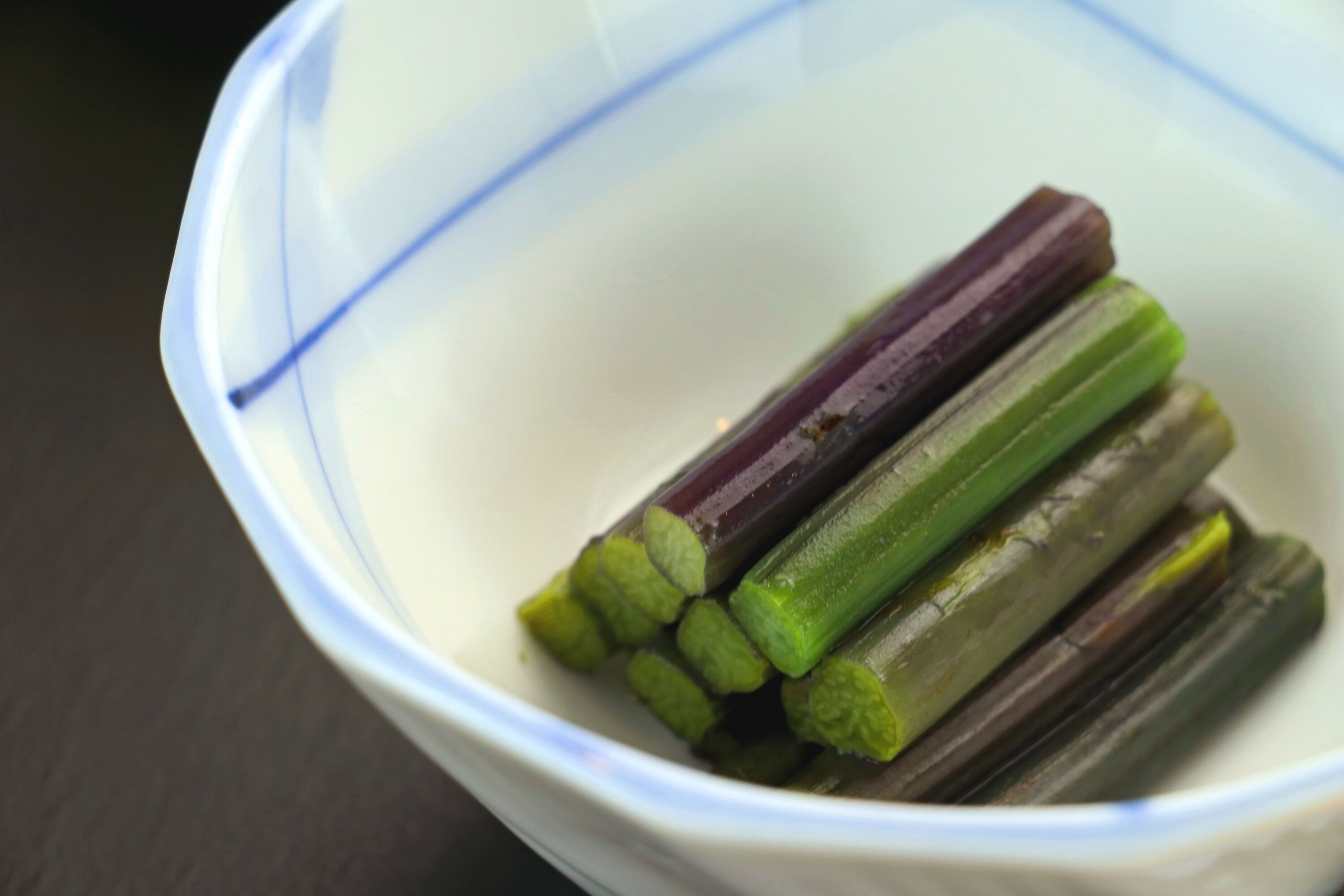 Un tazón con varios tallos de vegetales morados y verdes.