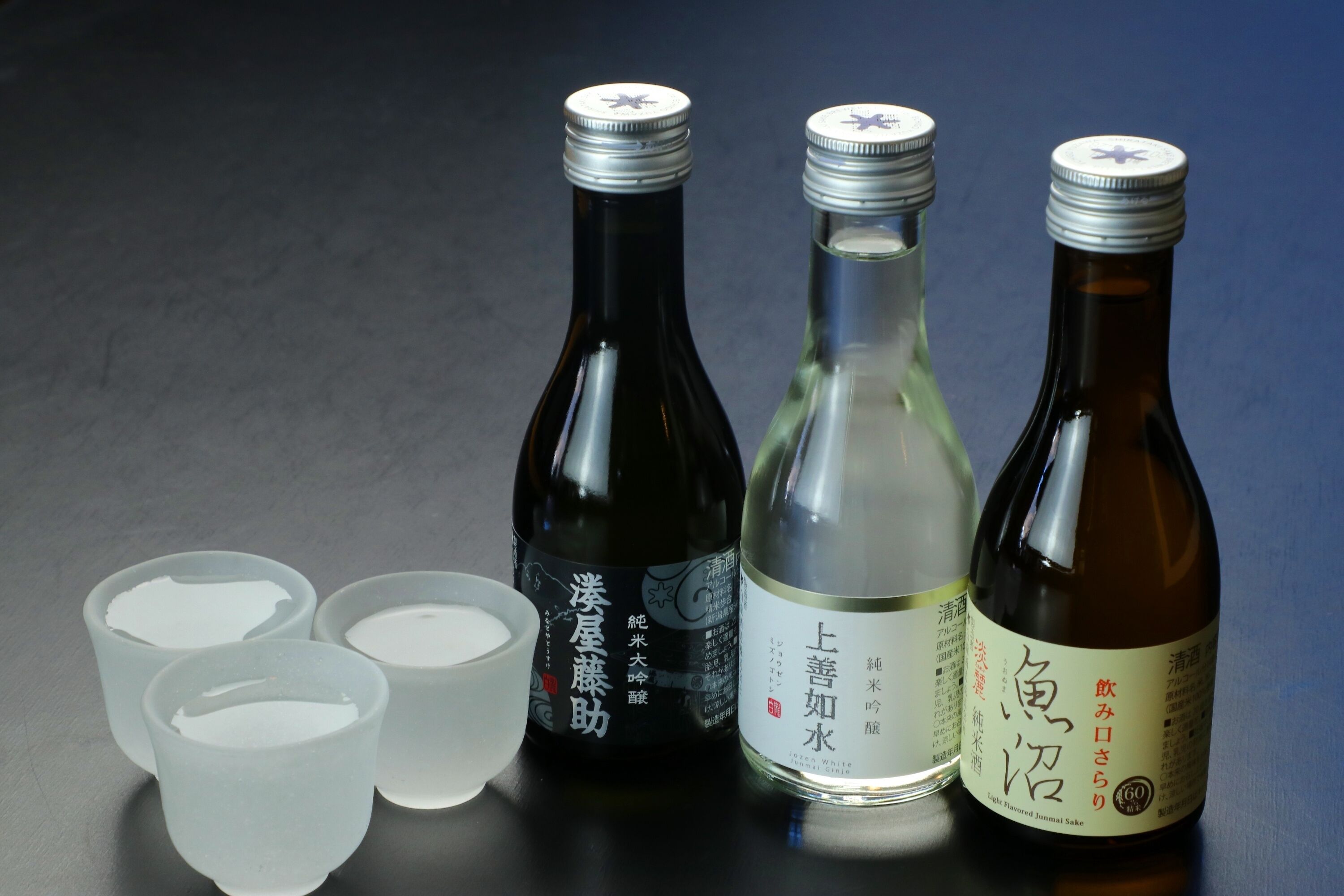 Three bottles of sake and three small cups on a table.