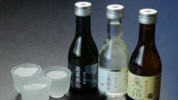 Three bottles of sake and three small cups on a table.