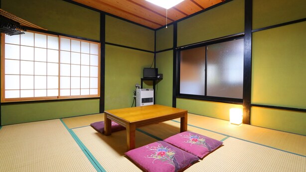 A tatami mat room with a wooden table and cushions, a TV, and a heater. - Warabisou (Yuzawa)