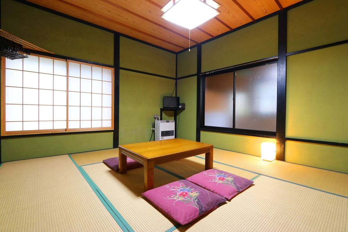 A tatami mat room with a wooden table and cushions, a TV, and a heater.
