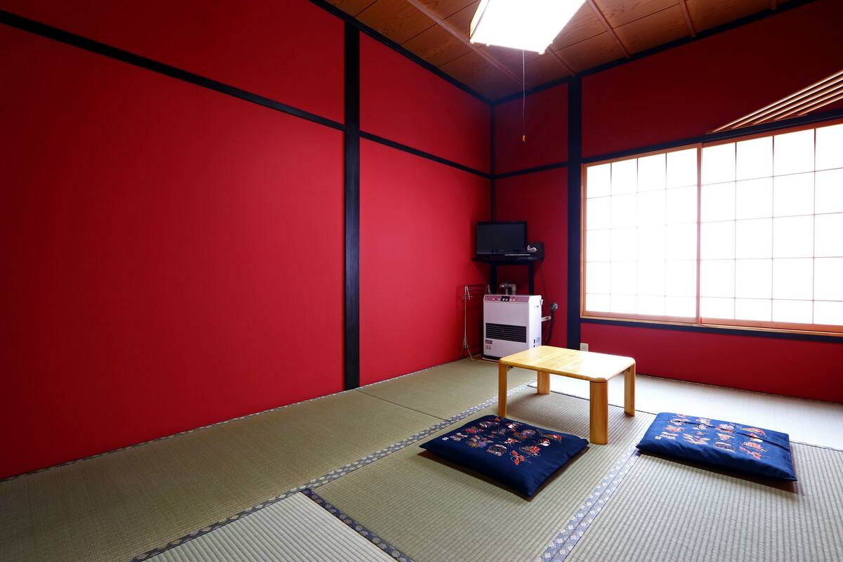 A tatami mat room with a wooden table and cushions, a heater, and a television on a cabinet.