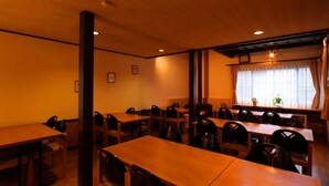 A restaurant with wooden tables and chairs, a fireplace, and a window with curtains. - Warabisou (Yuzawa)