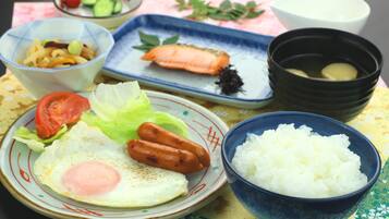 A table with various dishes including a plate with an egg, sausages, and vegetables, a bowl of rice, and a plate with salmon.