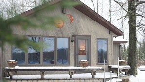 Une cabane en bois dotée de grandes fenêtres, d’un porche avec des bancs et d’un sol recouvert de neige.