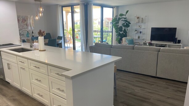 Eine moderne Küche mit einer großen Kochinsel, ein Essbereich mit Stühlen, eine Couch und ein Fernseher im Wohnzimmer.