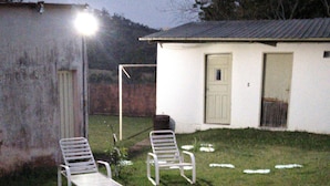 A small, single-story building with a white exterior and a flat roof. There are two white metal chairs in the front yard, and a single light post is visible. - 2 bedroom house near UNESP (Botucatu)