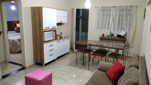A compact living space with a kitchenette, a dining area with a table and chairs, and a sofa with a red cushion. - 2 bedroom house near UNESP (Botucatu)